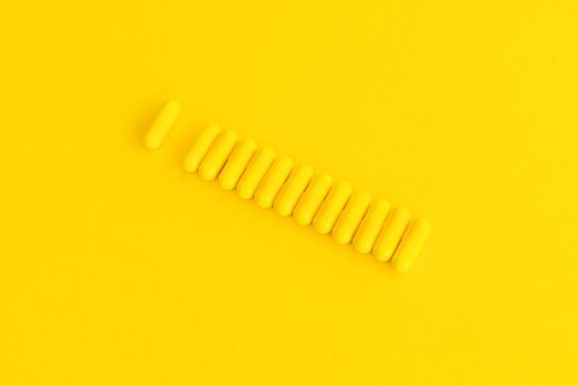 Twelve yellow capsules aligned on a solid yellow background, creating a striking monochromatic effect.