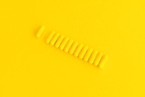 Free Twelve yellow capsules aligned on a solid yellow background, creating a striking monochromatic effect. Stock Photo