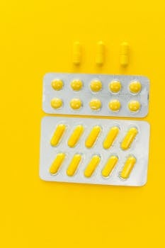 Vertical shot of yellow capsules and tablets in blister packs on a vibrant yellow background.