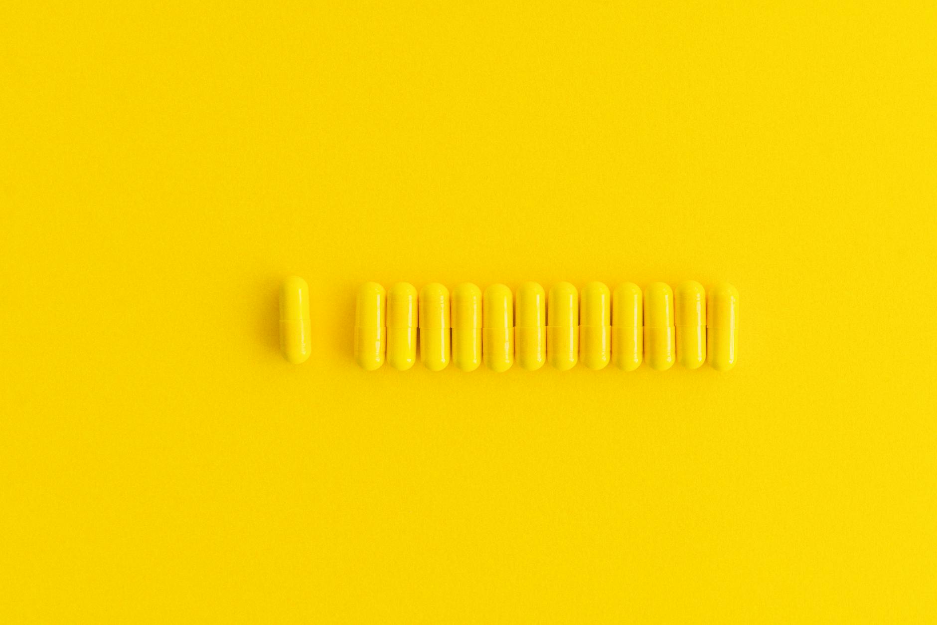 Close-up of yellow capsules lined up on a vibrant yellow background, perfect for healthcare themes.