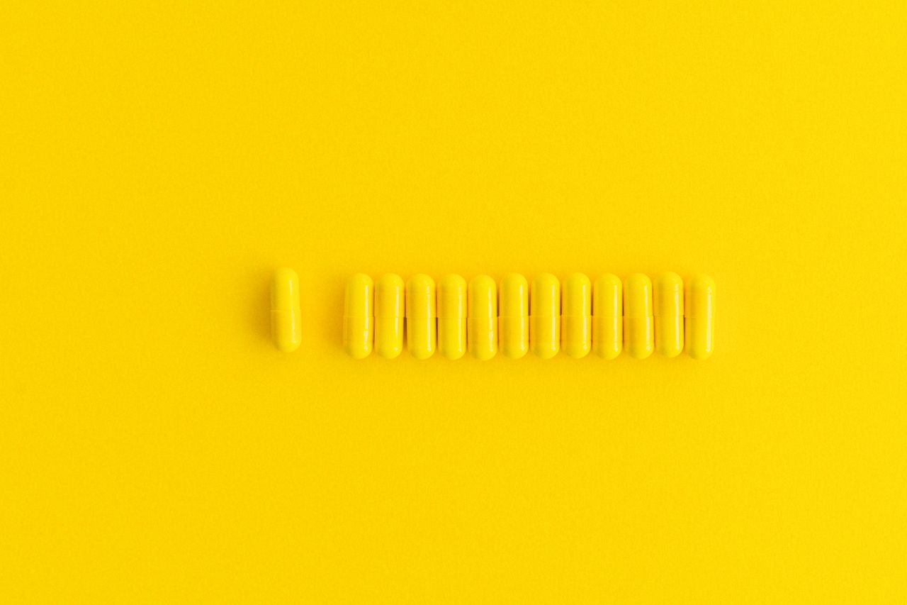 close up of yellow capsules lined up on a vibrant yellow background pe