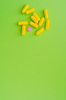 Flat lay of yellow capsules and one pink pill on a vivid green background.