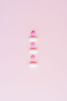 Close-up of pink and white pills lined up on a pastel pink background, emphasizing medication themes.