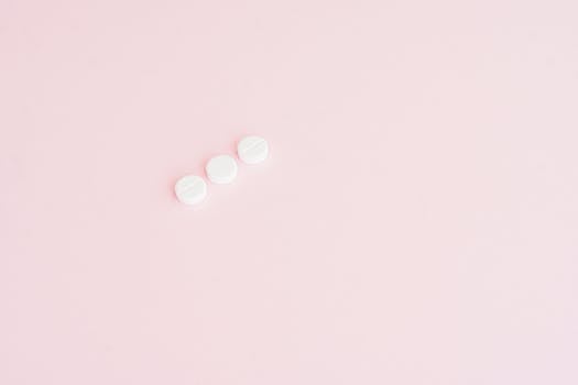 Simple minimalist image showing three white pills on a pastel pink background, ideal for health themes.
