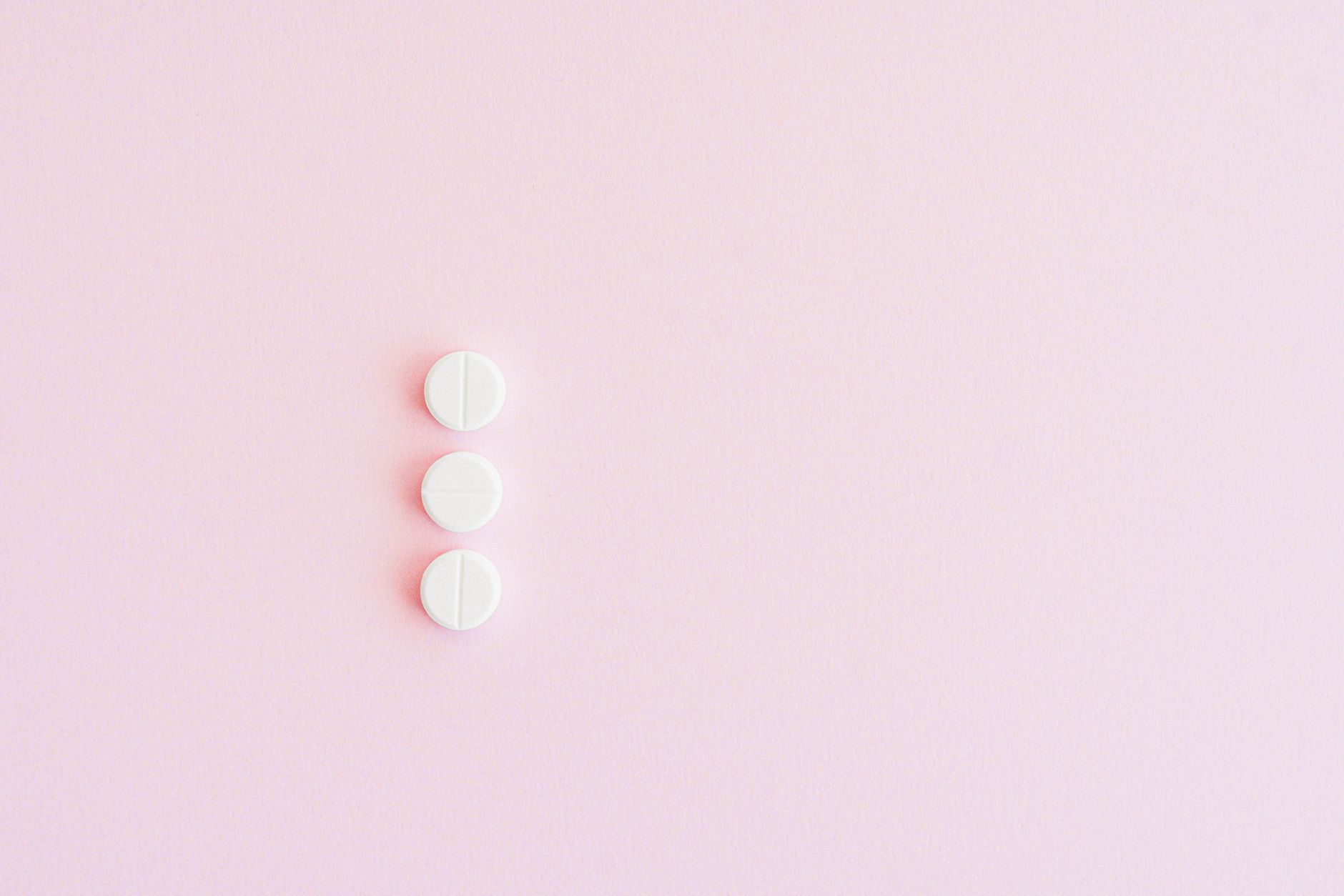 Three white pills arranged vertically on a pastel pink background for a minimalist medical concept.