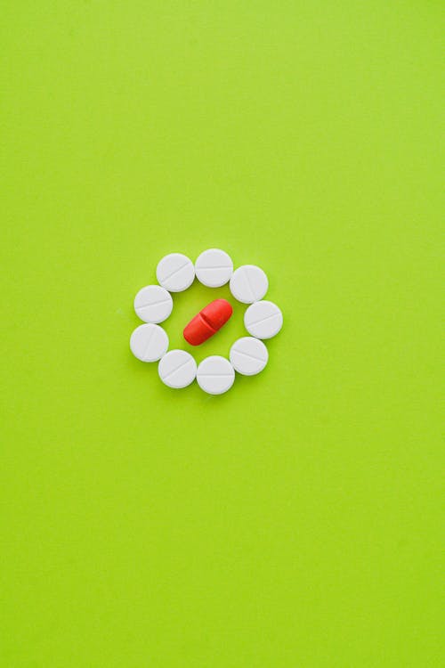 White Tablets and One Orange Tablet on Green Surface