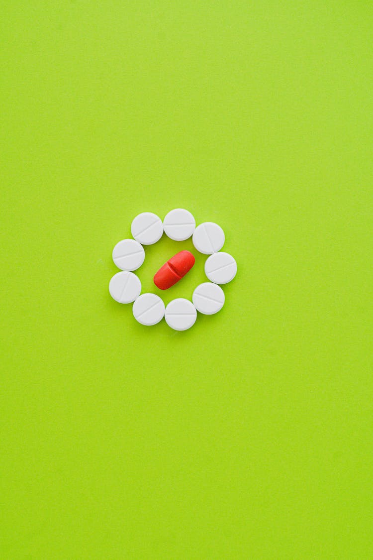 White Tablets And One Orange Tablet On Green Surface