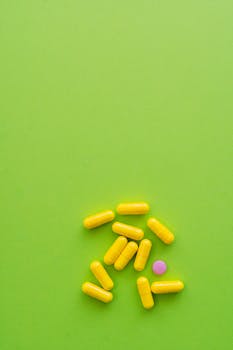 Yellow capsules and one pink pill on a bright green surface. Minimalist style.