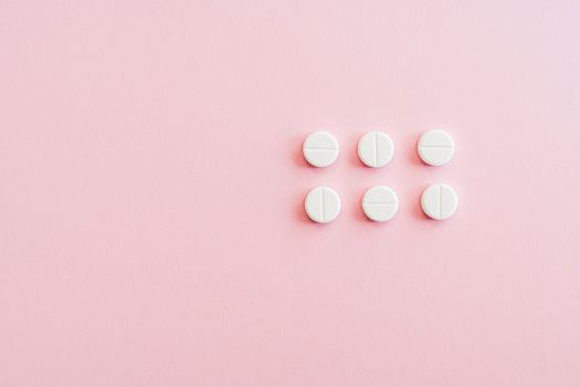 Minimalistic arrangement of white pills on a soft pink background.