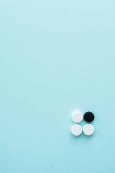 A minimalist flat lay of tablets on a baby blue background, featuring white and black pills.