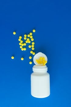 White container and scattered yellow pills on vibrant blue background.