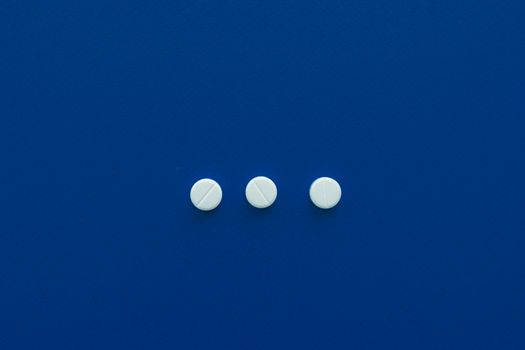 Three white pills arranged on a deep blue background for a minimalist look.