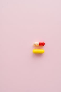 Red and yellow capsules placed on a soft pink background, showcasing a minimalist still life composition.