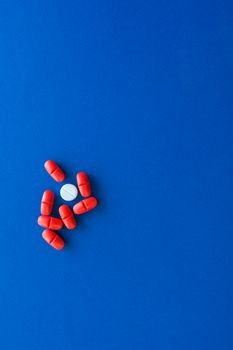 A minimalist image of red and white pills arranged on a vibrant blue background.