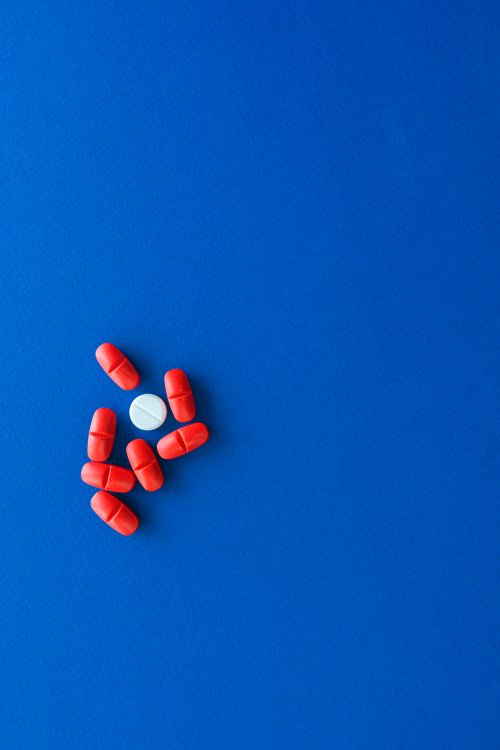Free A minimalist image of red and white pills arranged on a vibrant blue background. Stock Photo