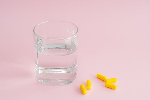 Glass of Water and Yellow Medicine Capsules