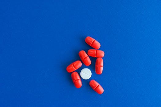 Close-up of red tablets surrounding a single white pill on a blue surface.