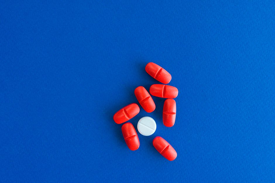 Close-up of red tablets surrounding a single white pill on a blue surface.
