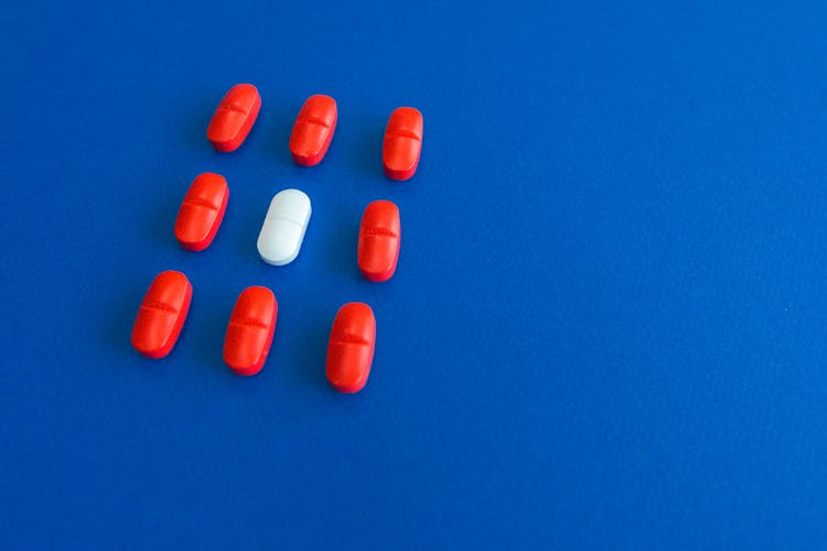 Red Tablets And One White Tablet On Blue Surface