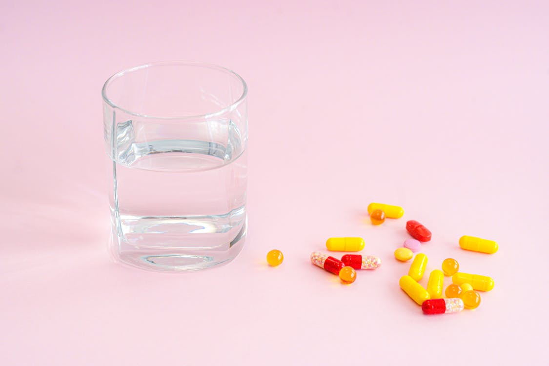 Free Clear Drinking Glass With Yellow and Pink Tablets Stock Photo