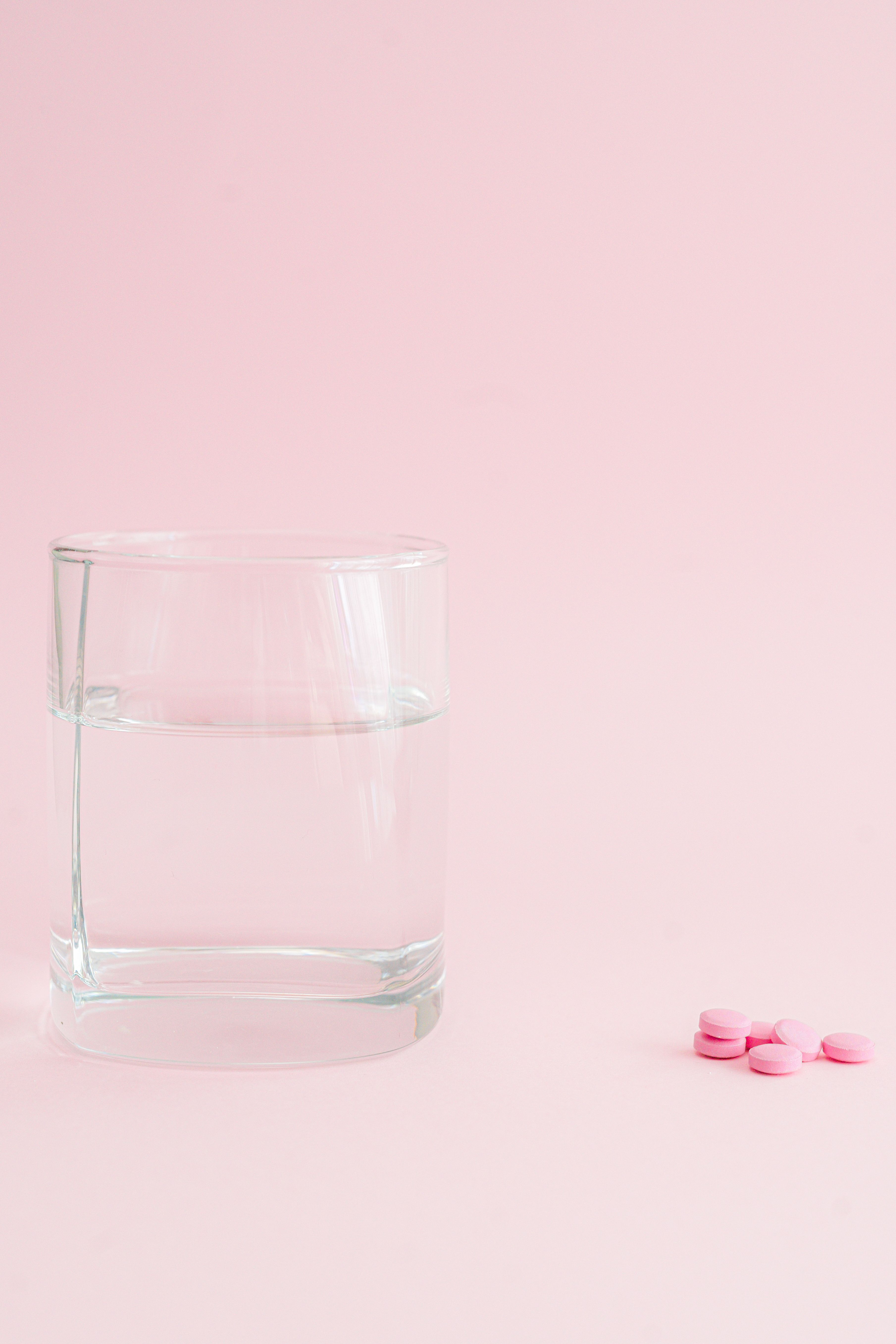 glass of water and pink pills in pink background
