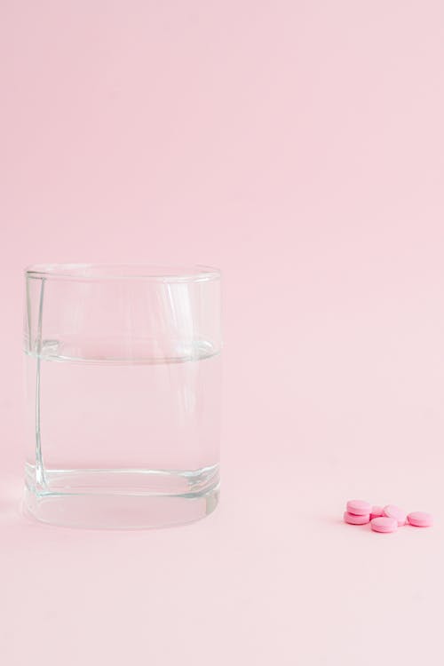 Glass of Water and Pink Pills in Pink Background