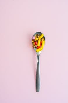 A spoon filled with assorted colorful pills placed on a pink background, offering a vibrant and minimalist composition.