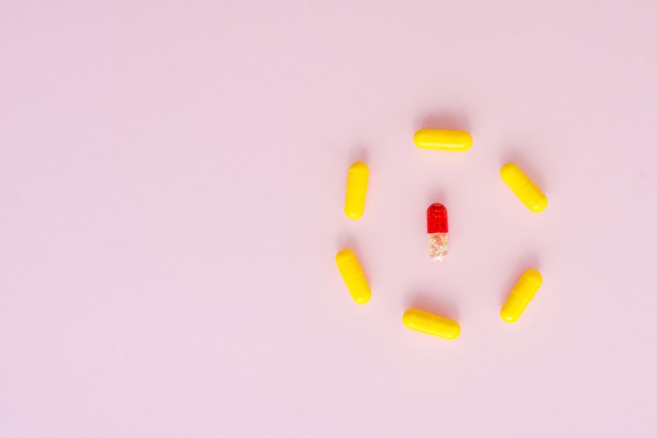Bright yellow and red capsules arranged on a pastel pink background.