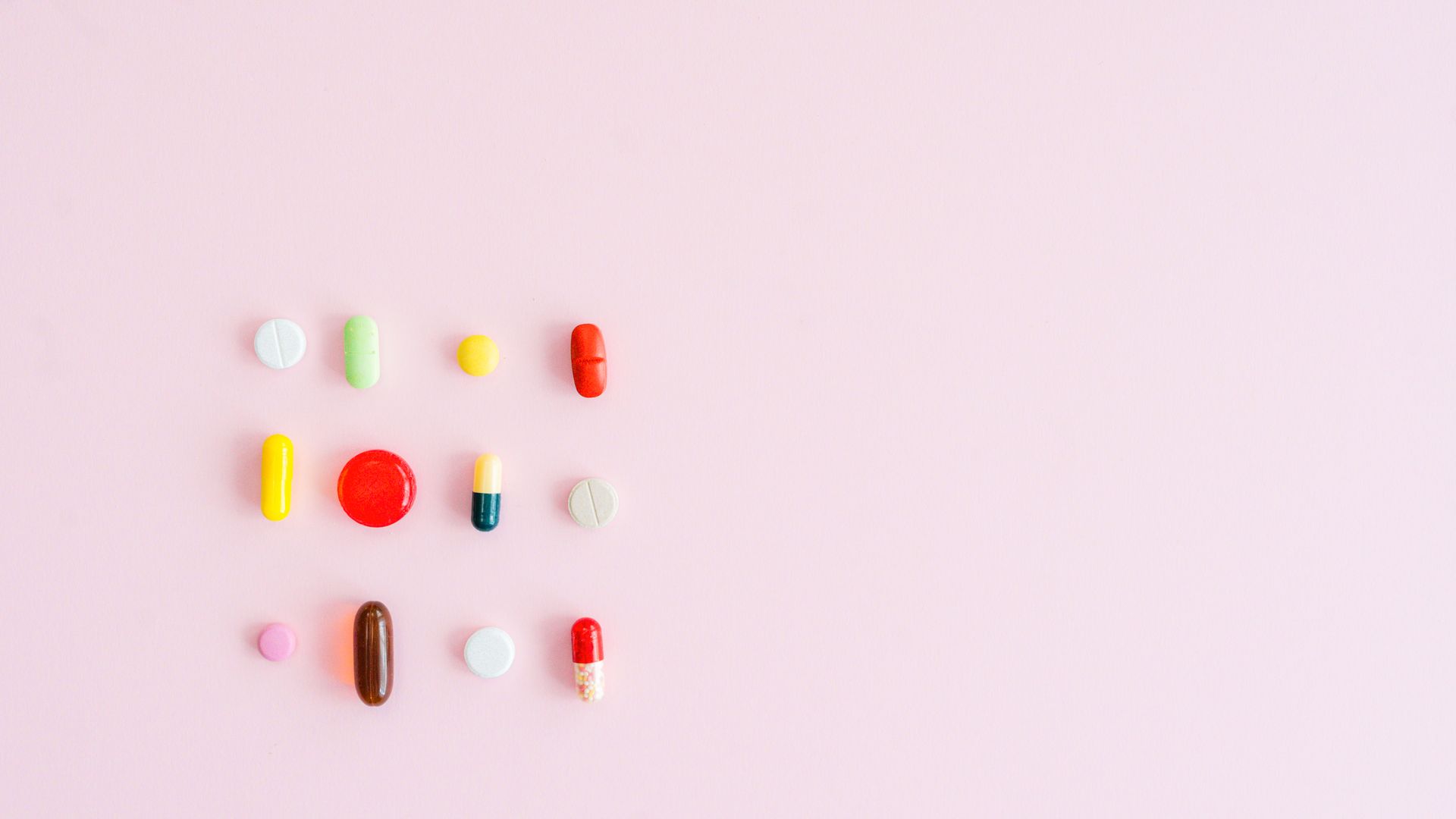 Modafinil for Memory Enhancement: Boost Your Brain Power Colorful assortment of pills and capsules arranged on a pastel pink background, perfect for healthcare themes.