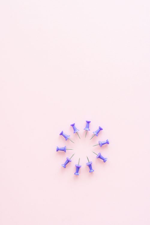 Free Close-up of purple push pins in a circular formation on a light pink background. Minimalist design. Stock Photo