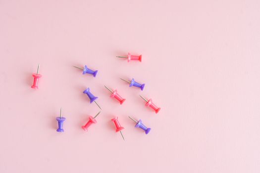 Vibrant red and purple thumbtacks scattered artfully on a pastel pink background.