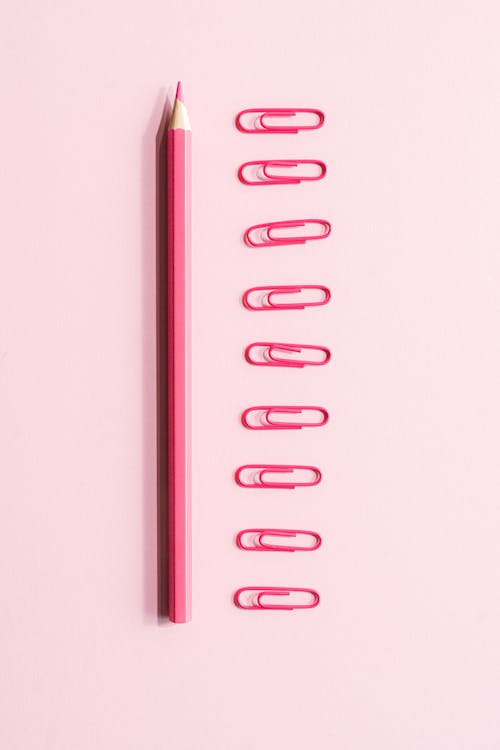 A Color Pencil and Paper Clips on Pink Surface