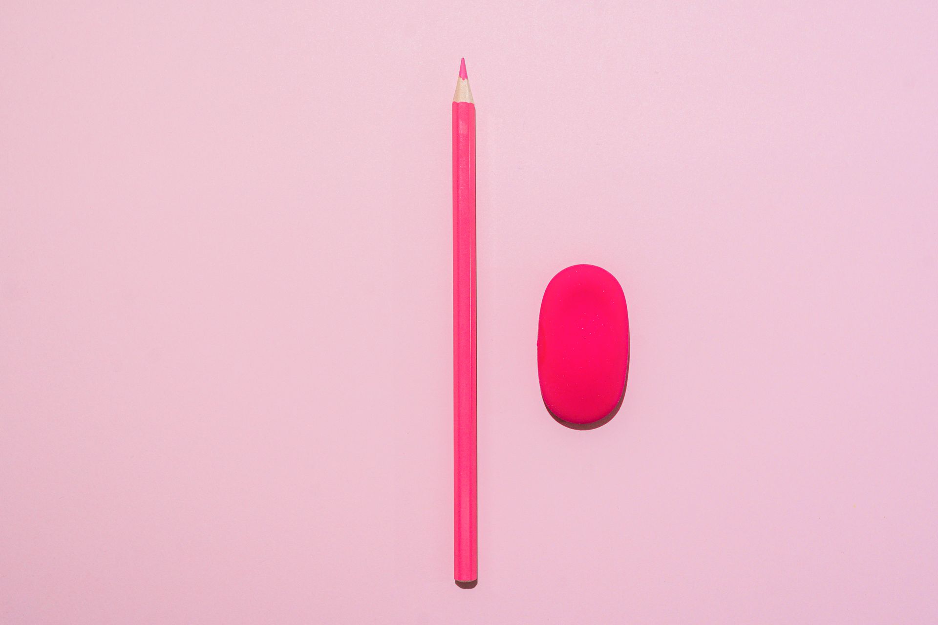 A pink colored pencil and eraser on a minimalist pink background, showcasing simplicity and school supplies.