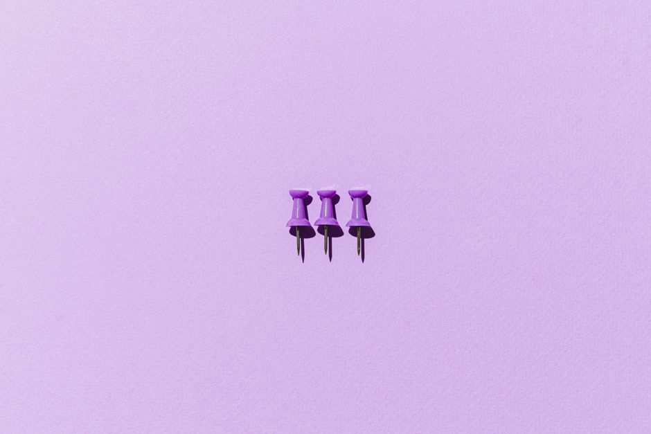 Close-up of purple thumb tacks on a pastel background for minimalist design concepts.