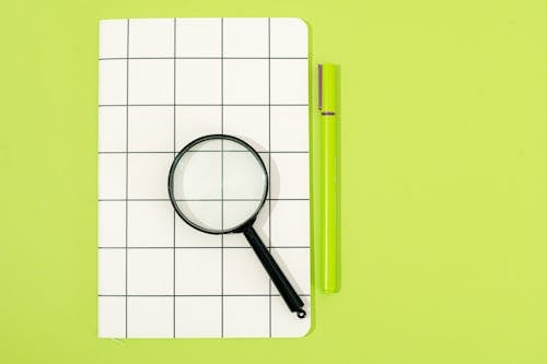 A Magnifying Glass on a Graphing Paper and Green Pen
