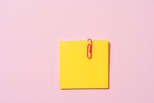 Free A vibrant yellow sticky note with a pink paper clip on a pastel pink backdrop, offering ample copyspace. Stock Photo