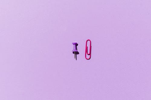 Pink Paper Clip and Purple Push Pin on Purple Background