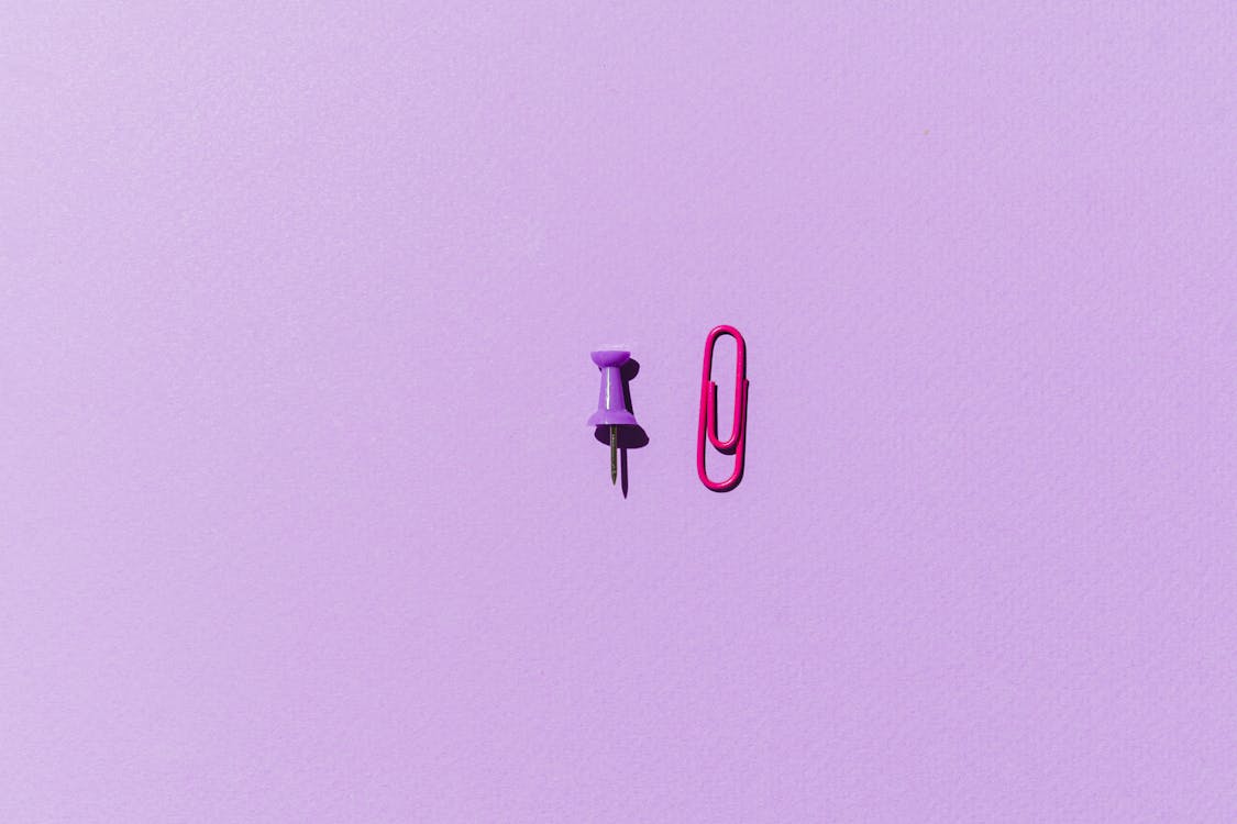 Pink Paper Clip and Purple Push Pin on Purple Background