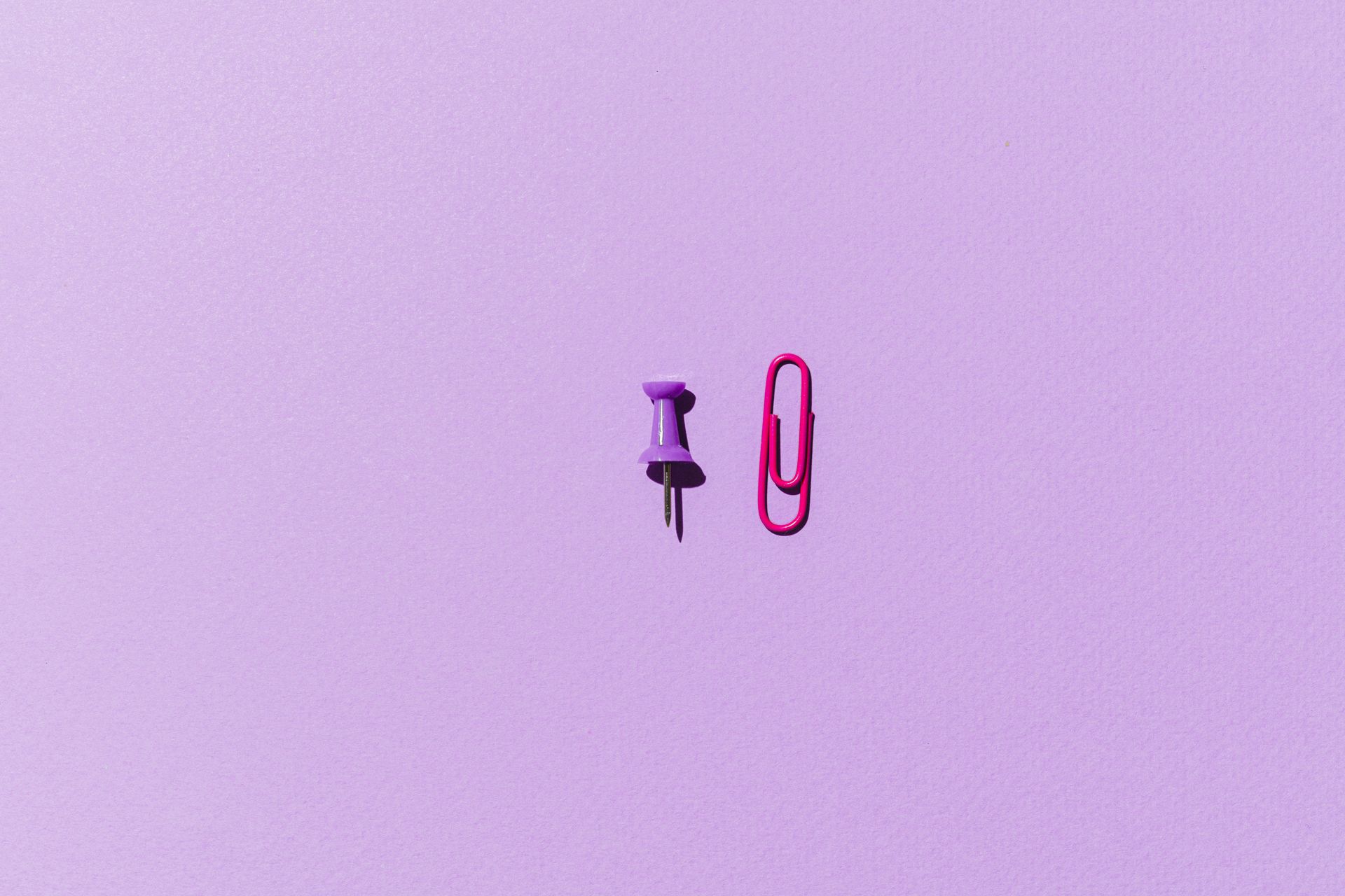 Pink Paper Clip and Purple Push Pin on Purple Background