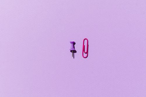 Free A vibrant flat lay of a purple push pin and pink paperclip on a pastel purple background. Stock Photo