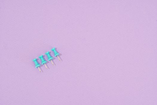 Four teal push pins arranged on a purple surface with ample copy space.