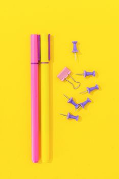 Bright and colorful pens with office supplies on a vibrant yellow surface.