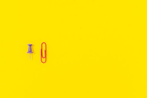 Free Purple Pushpin and Red Paper Clip on Yellow Background Stock Photo
