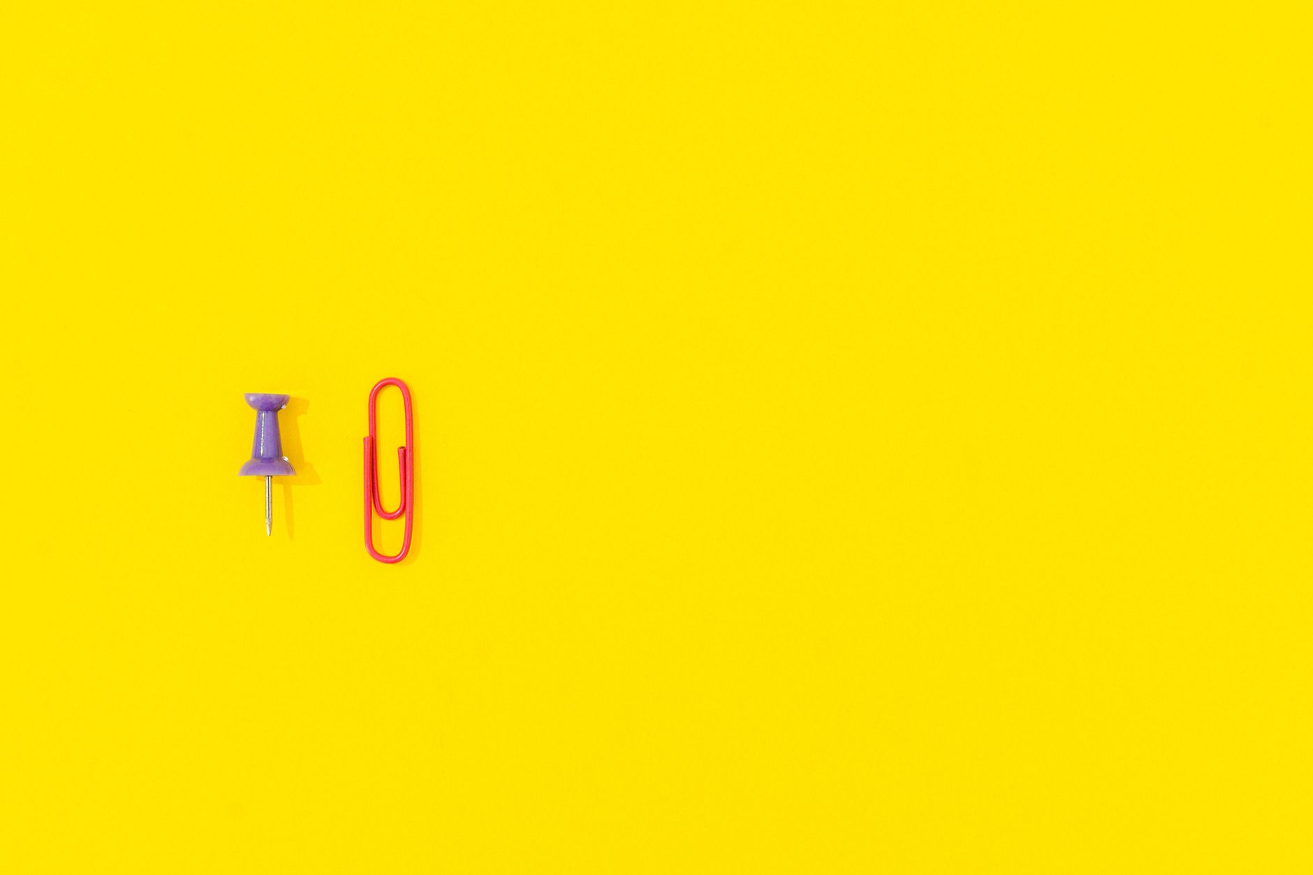 A minimalist arrangement of a push pin and paper clip on a bright yellow background, ideal for designs with copy space.