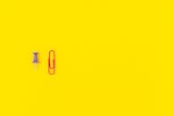 Purple Pushpin and Red Paper Clip on Yellow Background