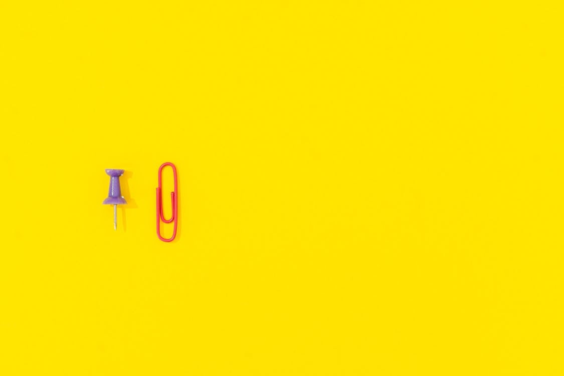 Purple Pushpin and Red Paper Clip on Yellow Background