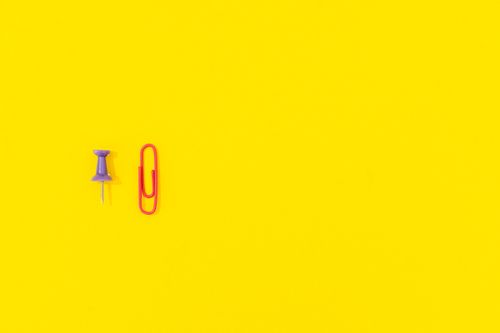 Free A minimalist arrangement of a push pin and paper clip on a bright yellow background, ideal for designs with copy space. Stock Photo