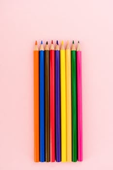 A colorful set of pencils neatly arranged on a light pink surface.