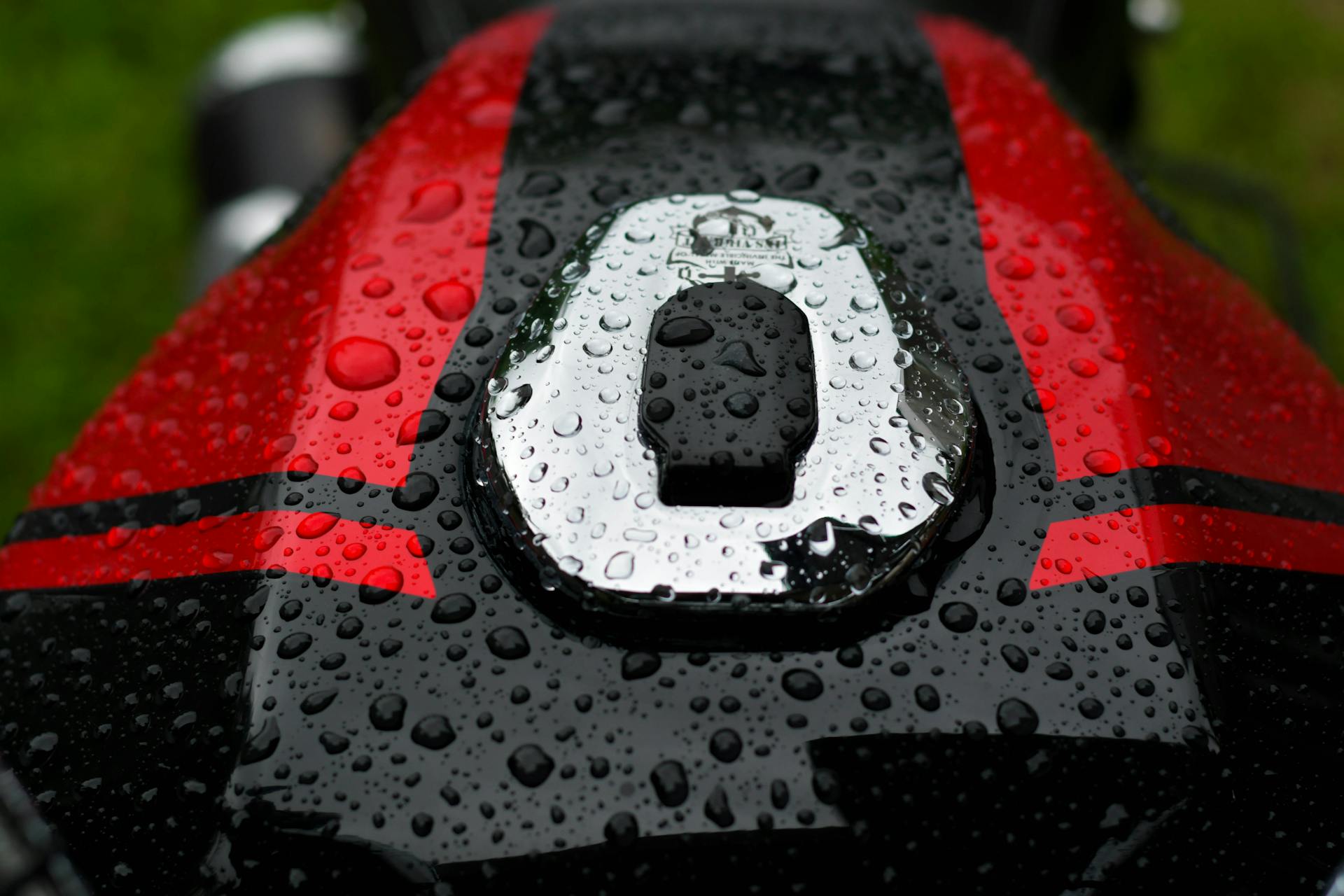 Close-up of raindrops on motorcycle fuel tank with red and black stripes, in Kandy, Sri Lanka.