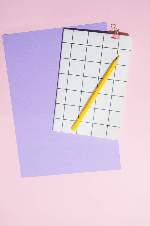 Free Top view of a notebook with grid pattern, yellow pencil, and paper on pink background. Stock Photo